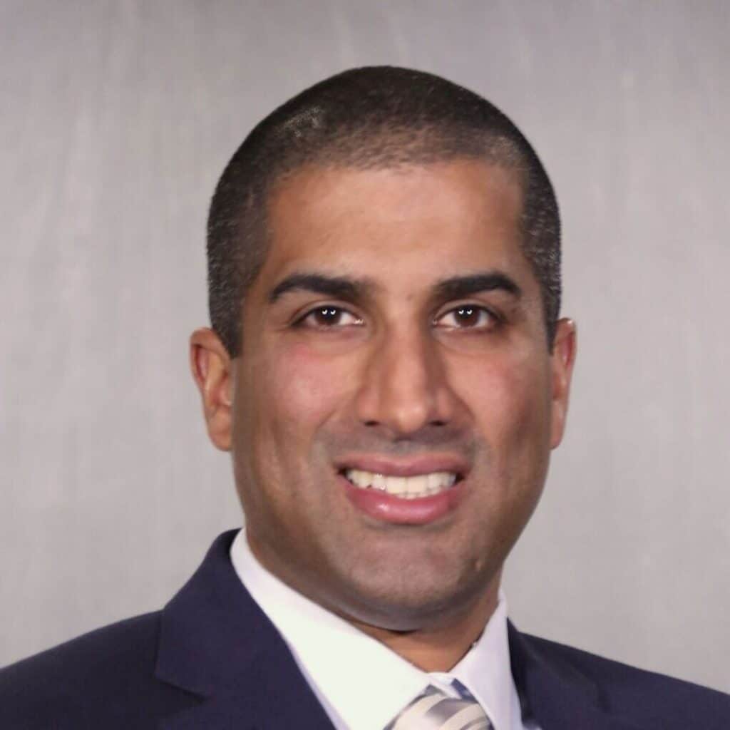 A man with short-cropped hair, wearing a dark suit, white shirt, and striped tie, smiling in front of a plain, light-colored background. C3 Solutions