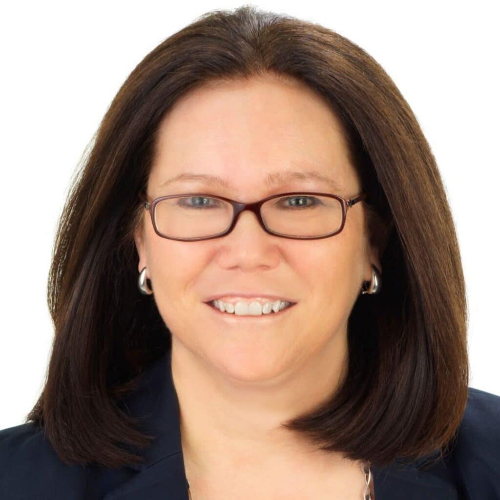 A woman with straight brown hair, wearing glasses, silver hoop earrings, and a dark blazer, smiling against a plain white background. C3 Solutions