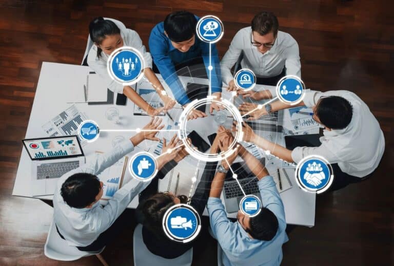 Un groupe hétérogène de collègues assis autour d'une table de réunion, les mains jointes au centre, entourés d'un graphique en forme de toile d'araignée illustrant la collaboration au sein de la chaîne d'approvisionnement. C3 Solutions