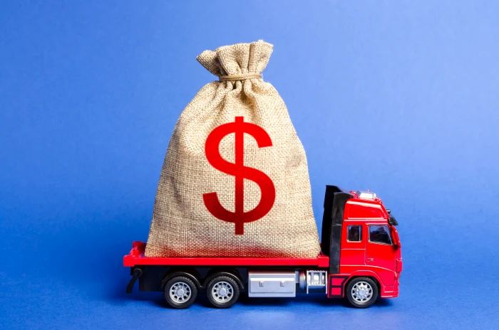 Un grand sac en toile de jute orné d'un signe $ rouge, posé sur la plate-forme d'un camion rouge miniature, symbolisant la retenue de marchandises. C3 Solutions