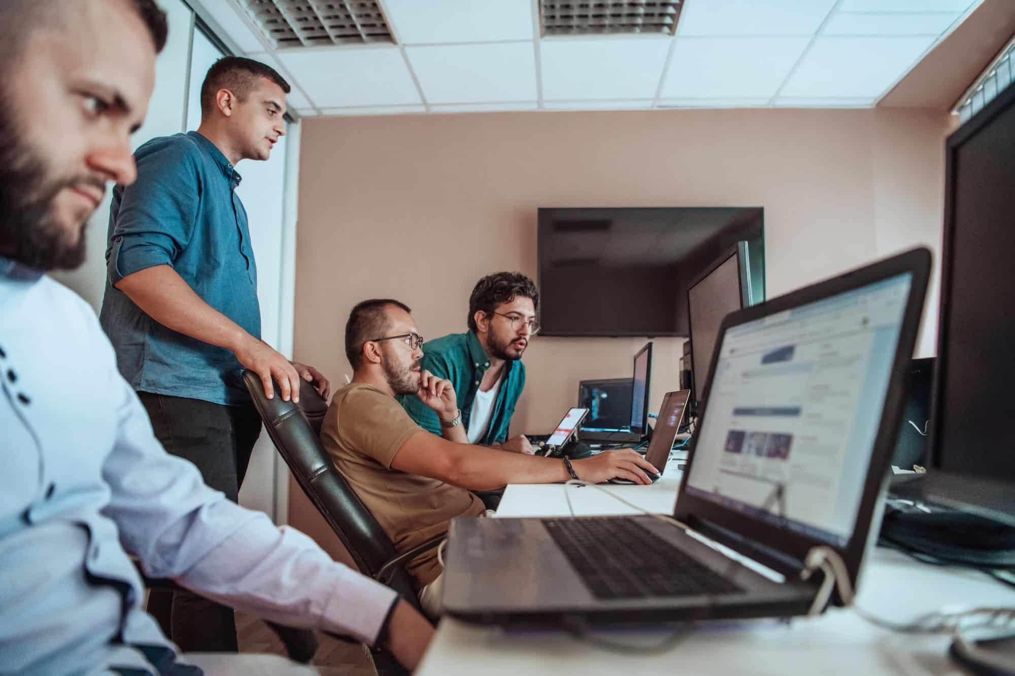 Four men collaborating at a workspace with multiple laptops and computer monitors to manage dock scheduling. C3 Solutions